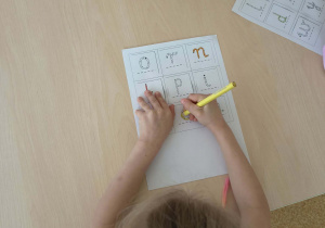 Dziewczynka koloruje literę na planszy do gry "Literowe BINGO"