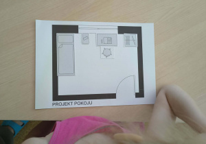 Dziewczynka projektuje na kartonie ustawienie mebli w pokoju dziecięcym