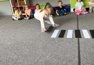 Dziewczynka dokłada pasek czarnego papieru, by ułożyć na dywanie przejście dla pieszych