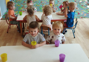 Sala przedszkolna. Dzieci siedzą przy stołach i degustują soki.
