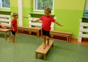 Dziewczynka wykonuje ćwiczenie równoważne na ławeczce