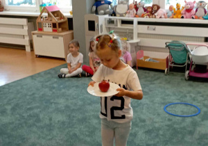 Dziewczynka podczas pokonywania toru przeszkód z jabłkiem na talerzu