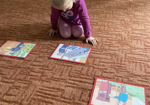 Dziewczynka na dywanie przygląda się ilustracji dotyczącej poczty