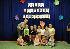 Dzieci z paniami pozują do zdjęcia na tle dekoracji z okazji Dnia Edukacji Narodowej