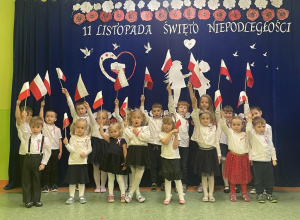 dzieci z flagami przed dekoracją z okazji Dnia Niepodległości