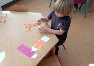 Chłopiec smaruje klejem kawałek kolorowego papieru, którym wykleja szablon kredki
