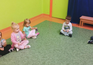 Sala gimnastyczna. Dzieci siedzą na podłodze, grają na różnych instrumentach.