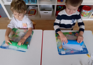 Sala przedszkolna. Dwóch chłopców siedzi przy stoliku i zwijają pomalowane kartony.
