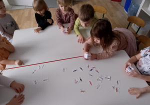 Sala przedszkolna. Dzieci wybierają z rozrzuconych na stole ilustracji, wylosowany przez siebie obrazek.