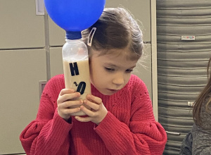 dziewczynka słucha jak pracują drożdże w butelce