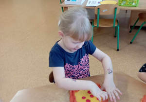 Dziewczynka wylepia plasteliną kartonową pizzę